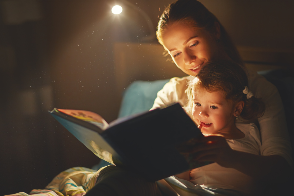 mama en dochter die in bed lezen met een lampje